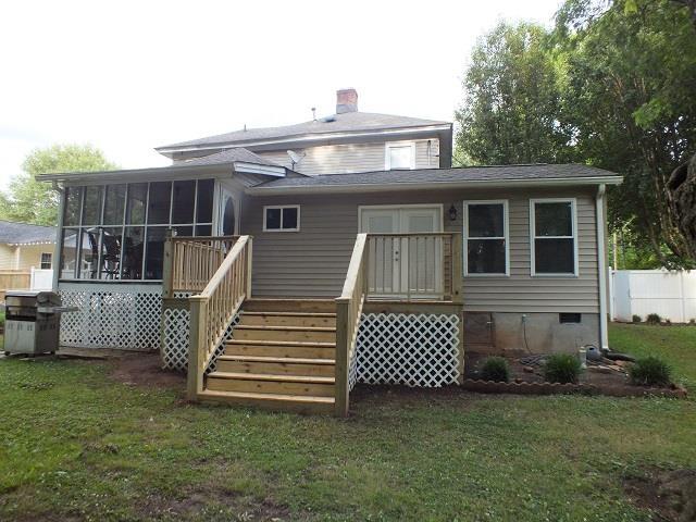 back of property with a wooden deck, a sunroom, and a lawn