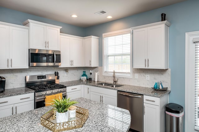 kitchen featuring light stone countertops, appliances with stainless steel finishes, sink, white cabinets, and tasteful backsplash