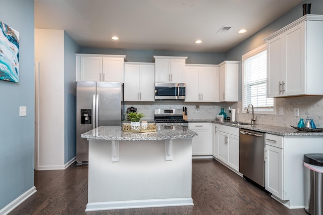 kitchen with dark hardwood / wood-style floors, white cabinets, a kitchen island, and appliances with stainless steel finishes