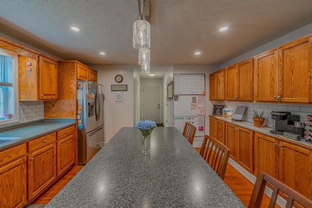 kitchen with hanging light fixtures, stainless steel refrigerator with ice dispenser, tasteful backsplash, and hardwood / wood-style flooring