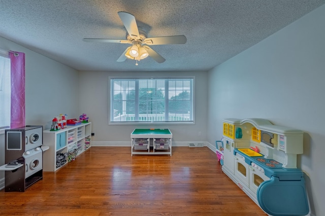 recreation room with ceiling fan, a textured ceiling, and dark wood-type flooring