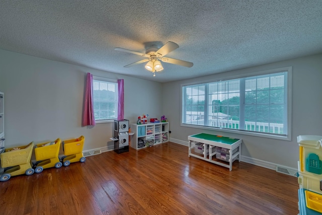 recreation room with a textured ceiling, a healthy amount of sunlight, ceiling fan, and dark wood-type flooring