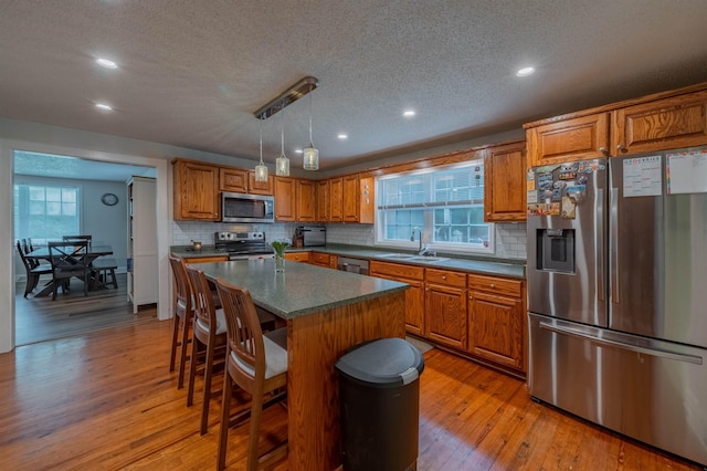 kitchen featuring appliances with stainless steel finishes, hanging light fixtures, a center island, a healthy amount of sunlight, and light hardwood / wood-style flooring