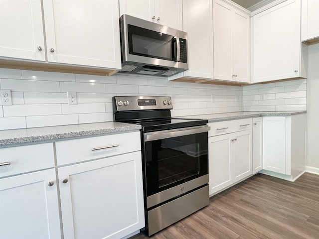 kitchen featuring appliances with stainless steel finishes, hardwood / wood-style floors, white cabinets, backsplash, and light stone counters