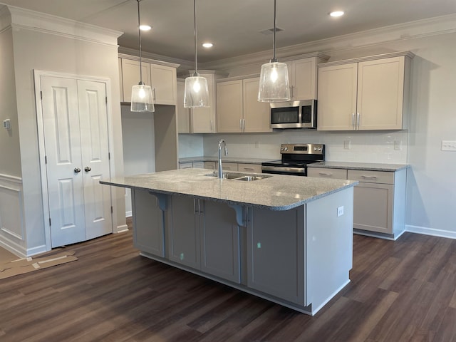 kitchen featuring sink, appliances with stainless steel finishes, light stone countertops, a center island with sink, and decorative light fixtures