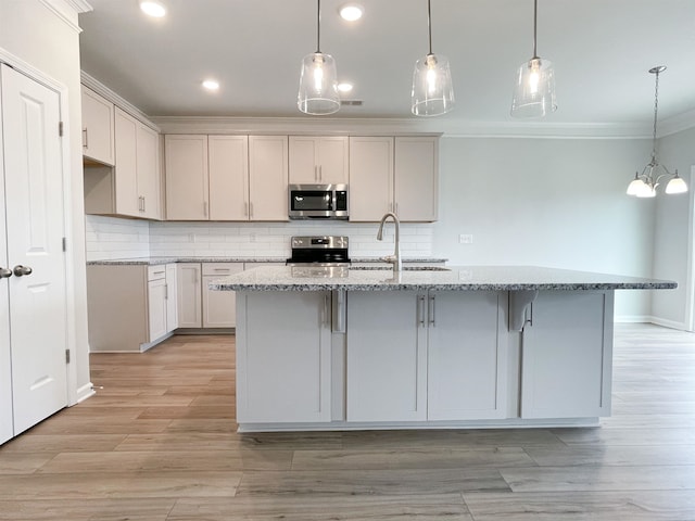 kitchen featuring crown molding, tasteful backsplash, stainless steel appliances, and a center island with sink