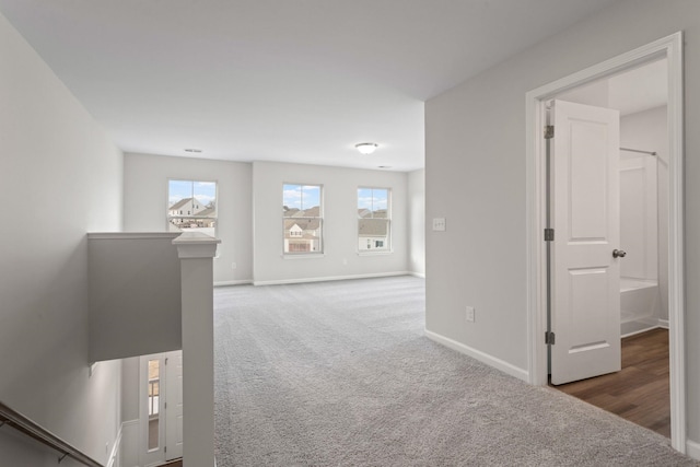 corridor with baseboards, an upstairs landing, and carpet flooring