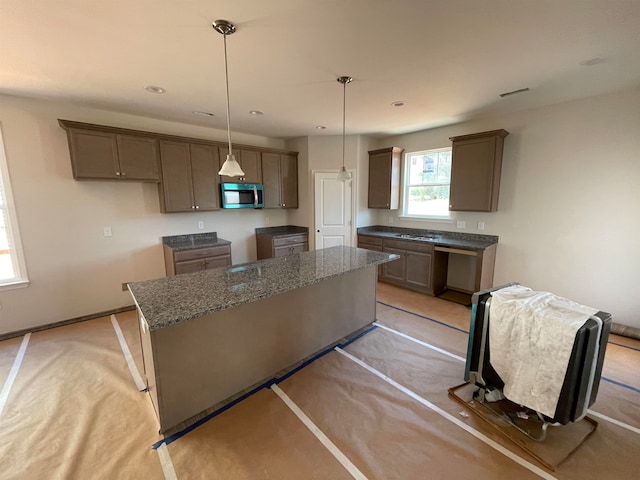 kitchen with stone countertops, a center island, light colored carpet, and hanging light fixtures