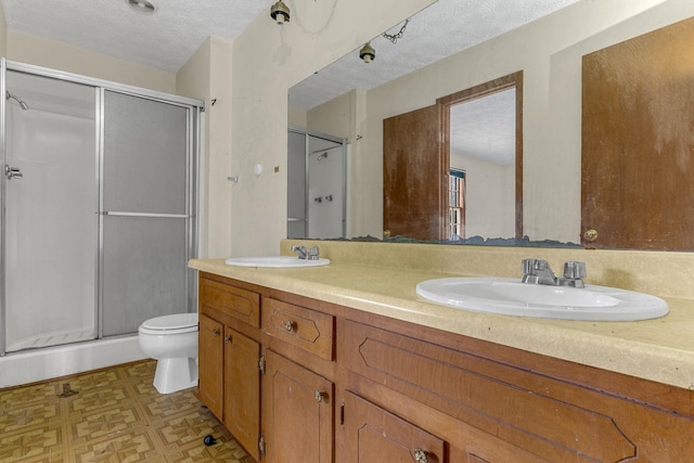 bathroom with a shower with shower door, large vanity, a textured ceiling, dual sinks, and toilet