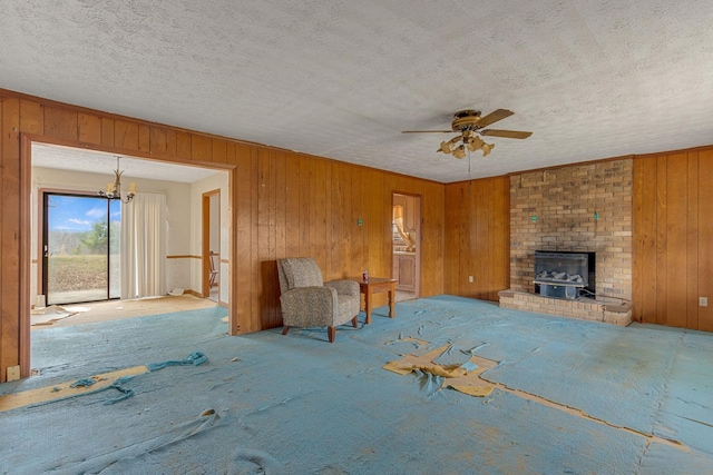 unfurnished living room with brick wall, a brick fireplace, light colored carpet, wood walls, and ceiling fan with notable chandelier