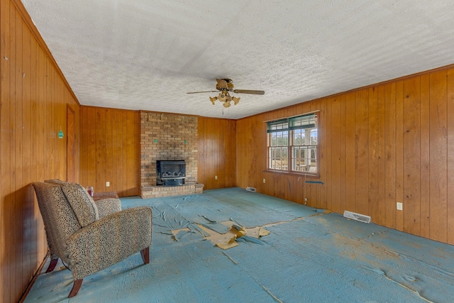 carpeted living room featuring ceiling fan, brick wall, a brick fireplace, a textured ceiling, and wooden walls