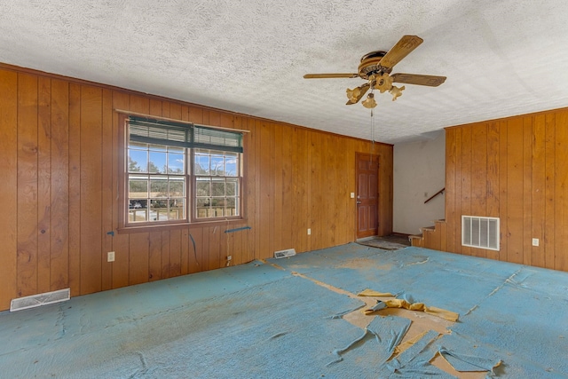 unfurnished room with carpet, wood walls, ceiling fan, and a textured ceiling