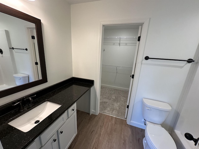 bathroom with a spacious closet, wood finished floors, vanity, and baseboards