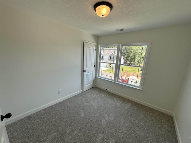 empty room with carpet floors, visible vents, a textured ceiling, and baseboards