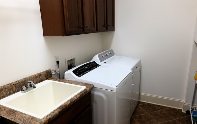 washroom featuring cabinet space, baseboards, washing machine and clothes dryer, dark tile patterned floors, and a sink