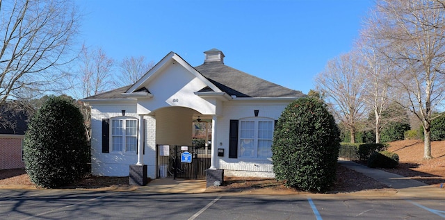 view of front facade featuring brick siding, a shingled roof, fence, and a gate