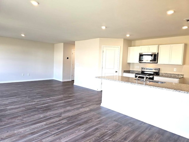 kitchen featuring white cabinets, stainless steel appliances, light stone counters, and dark wood-type flooring