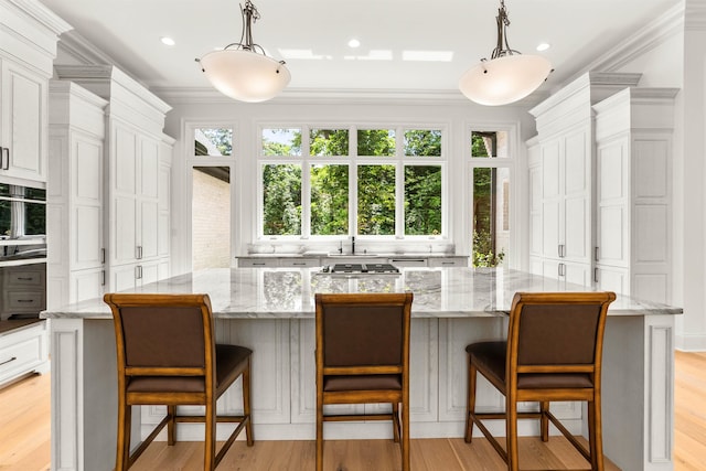 kitchen featuring light stone counters, light hardwood / wood-style flooring, pendant lighting, and a spacious island