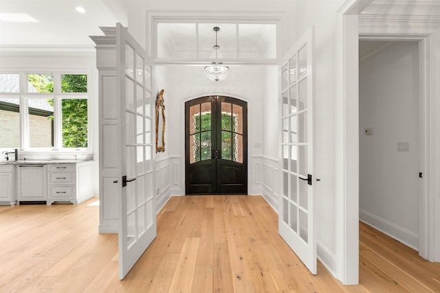 foyer entrance featuring french doors, ornamental molding, and light wood-type flooring