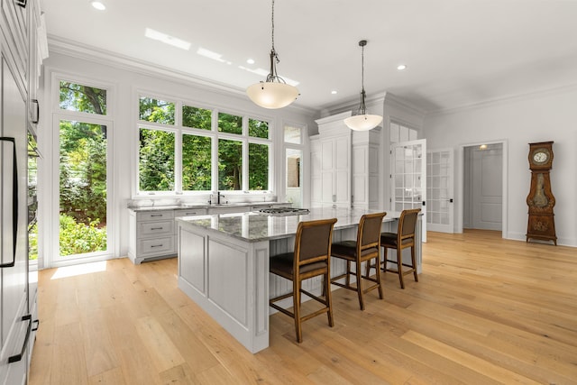 kitchen with a kitchen breakfast bar, pendant lighting, light hardwood / wood-style flooring, light stone counters, and a kitchen island