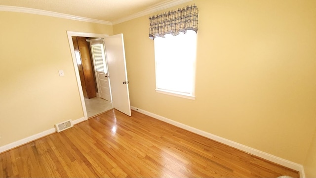 empty room with crown molding and light hardwood / wood-style floors