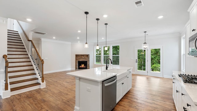 kitchen with sink, an island with sink, a fireplace, light hardwood / wood-style flooring, and appliances with stainless steel finishes