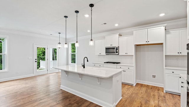 kitchen with white cabinets, a kitchen island with sink, light wood-type flooring, and decorative light fixtures