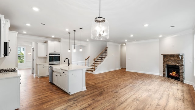 kitchen featuring hanging light fixtures, a stone fireplace, a kitchen island with sink, white cabinetry, and stainless steel appliances