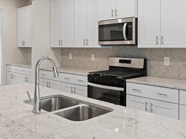 kitchen with gas stove, light stone countertops, sink, and white cabinets