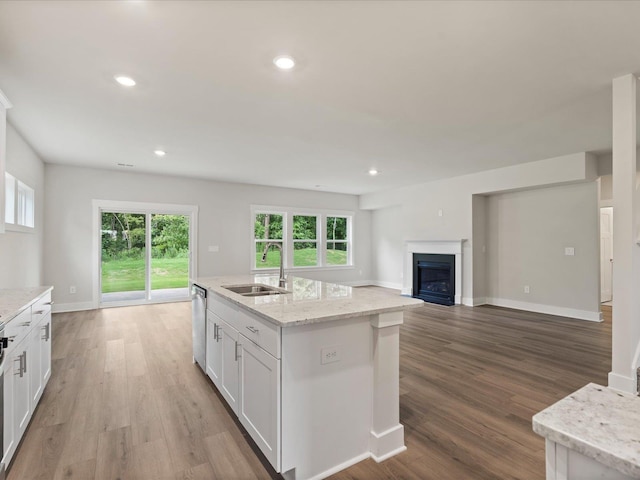 kitchen featuring light stone counters, a kitchen island with sink, sink, dishwasher, and white cabinets