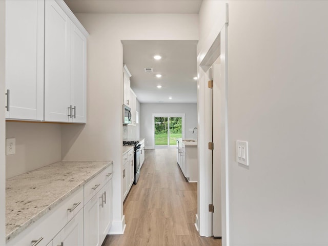 kitchen featuring light stone countertops, white cabinetry, stainless steel appliances, and light hardwood / wood-style flooring