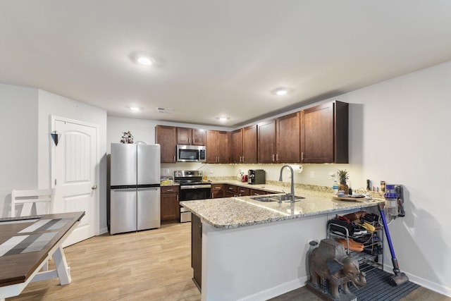 kitchen with sink, appliances with stainless steel finishes, light hardwood / wood-style floors, light stone countertops, and kitchen peninsula