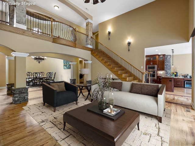 living room with ceiling fan, light wood-type flooring, a high ceiling, and ornate columns