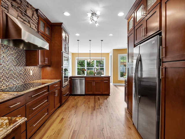 kitchen with sink, stainless steel appliances, wall chimney range hood, tasteful backsplash, and pendant lighting