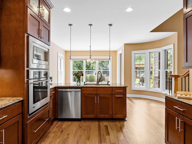 kitchen featuring light stone countertops, sink, light hardwood / wood-style flooring, decorative light fixtures, and appliances with stainless steel finishes