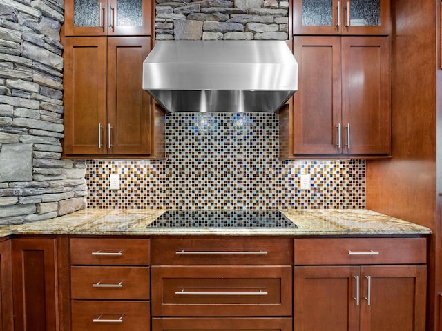 kitchen featuring black electric stovetop, backsplash, light stone counters, and wall chimney exhaust hood