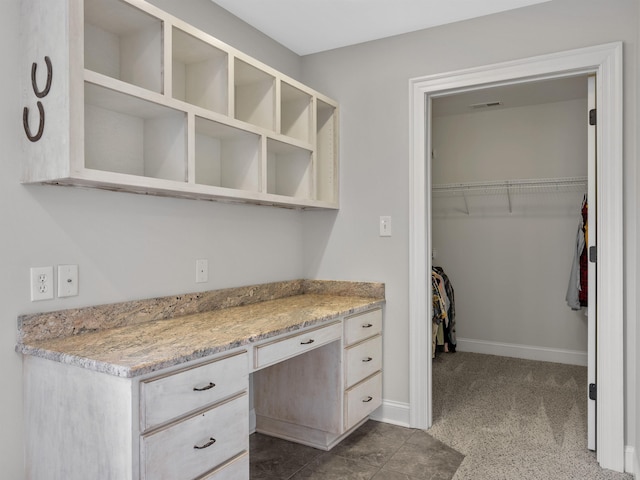 kitchen with dark carpet, light stone counters, and built in desk