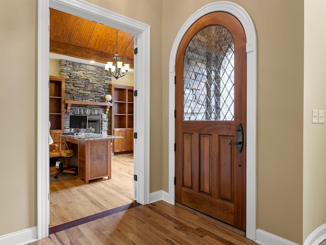 foyer entrance with a fireplace, beamed ceiling, a notable chandelier, light hardwood / wood-style floors, and wood ceiling