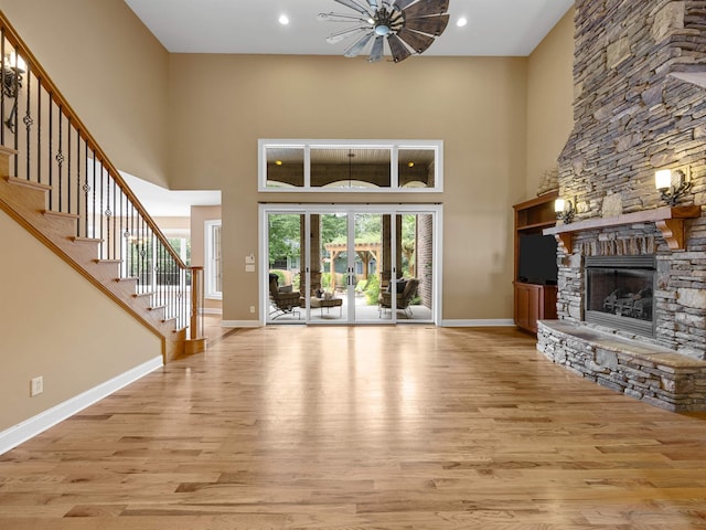 unfurnished living room featuring a stone fireplace, a towering ceiling, and light wood-type flooring