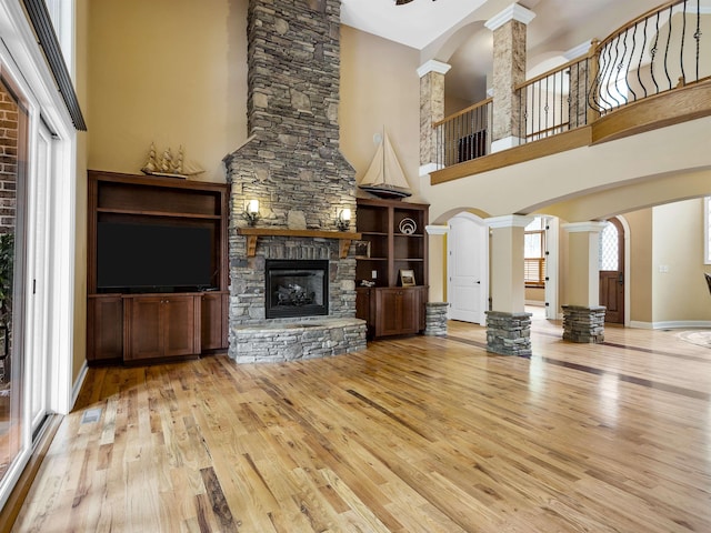 unfurnished living room featuring a stone fireplace, a towering ceiling, and decorative columns