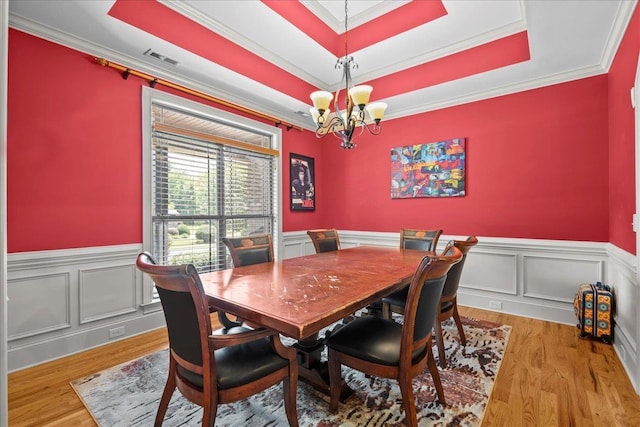 dining area featuring a tray ceiling, light hardwood / wood-style flooring, ornamental molding, and an inviting chandelier