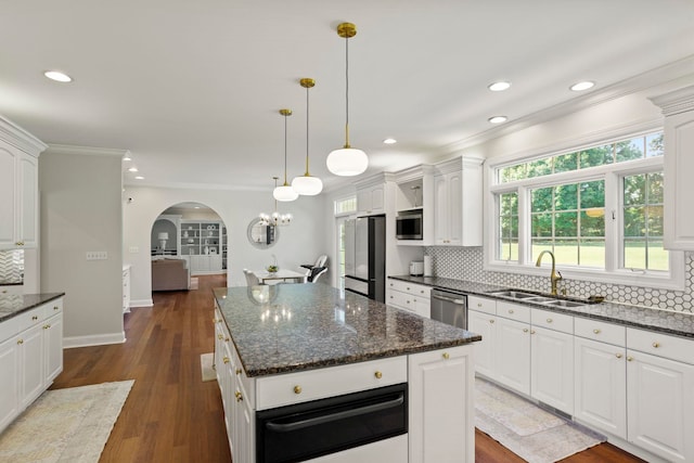 kitchen with dark wood-style floors, arched walkways, a warming drawer, appliances with stainless steel finishes, and a sink