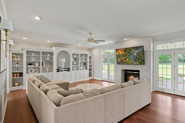 living area with dark wood-style flooring, crown molding, recessed lighting, ceiling fan, and a warm lit fireplace