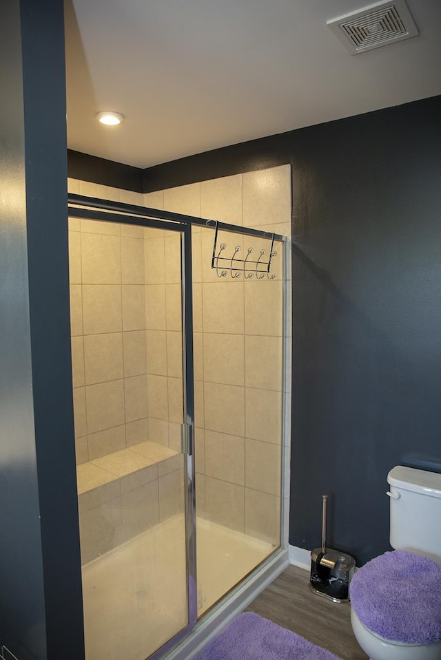 bathroom with hardwood / wood-style floors, toilet, and a shower with door