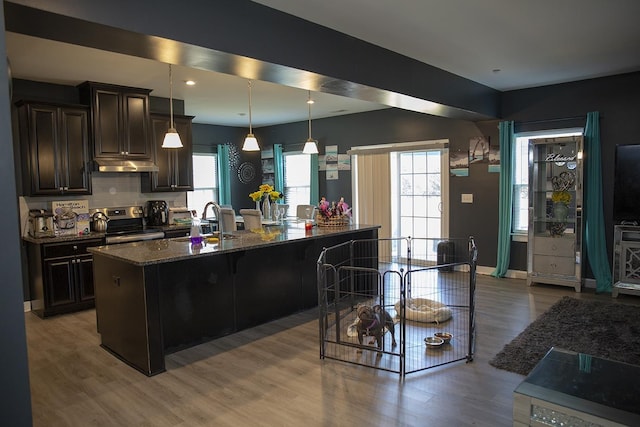 kitchen with dark stone counters, a breakfast bar, dark brown cabinetry, hardwood / wood-style floors, and stainless steel electric range