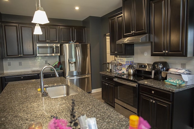 kitchen featuring appliances with stainless steel finishes, tasteful backsplash, dark stone counters, sink, and decorative light fixtures