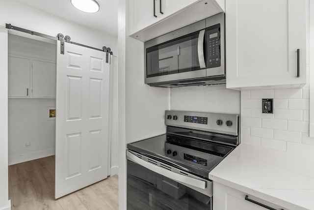 kitchen featuring white cabinetry, appliances with stainless steel finishes, a barn door, and light hardwood / wood-style floors