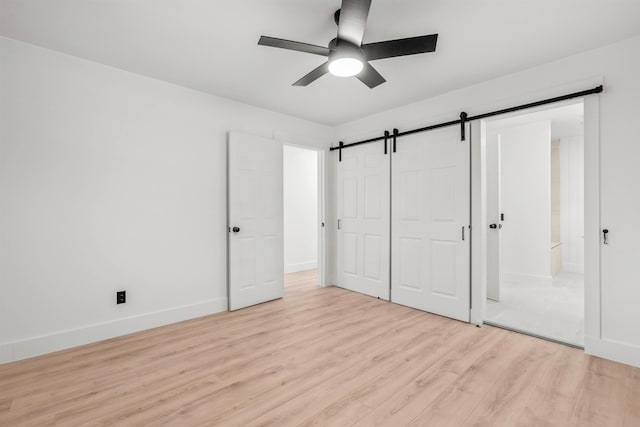 unfurnished bedroom with a closet, light hardwood / wood-style flooring, a barn door, and ceiling fan