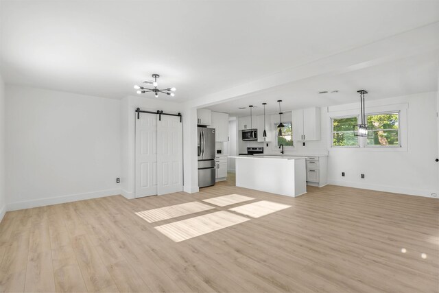 kitchen with stainless steel appliances, a center island, white cabinets, decorative light fixtures, and a barn door