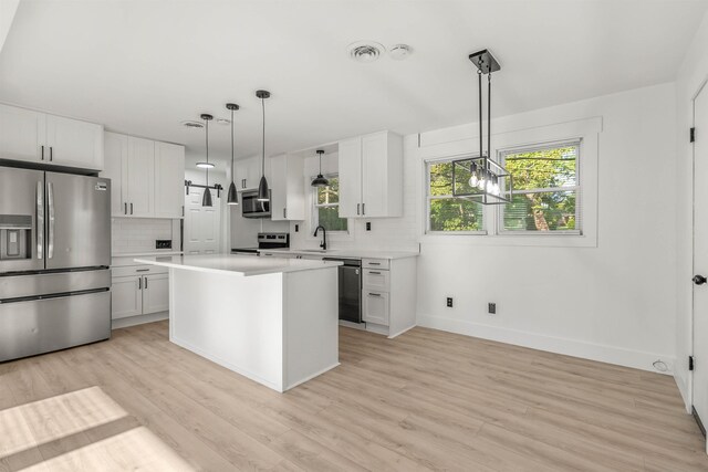 kitchen with white cabinetry, decorative light fixtures, a kitchen island, and appliances with stainless steel finishes